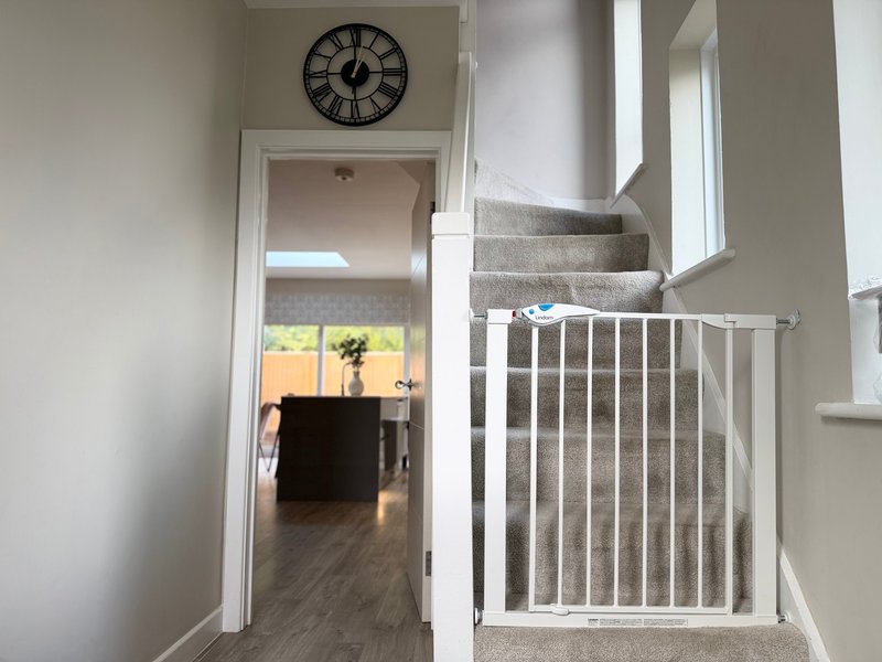 Hallway with carpeted stairs, white railing, wall clock, and view to kitchen beyond