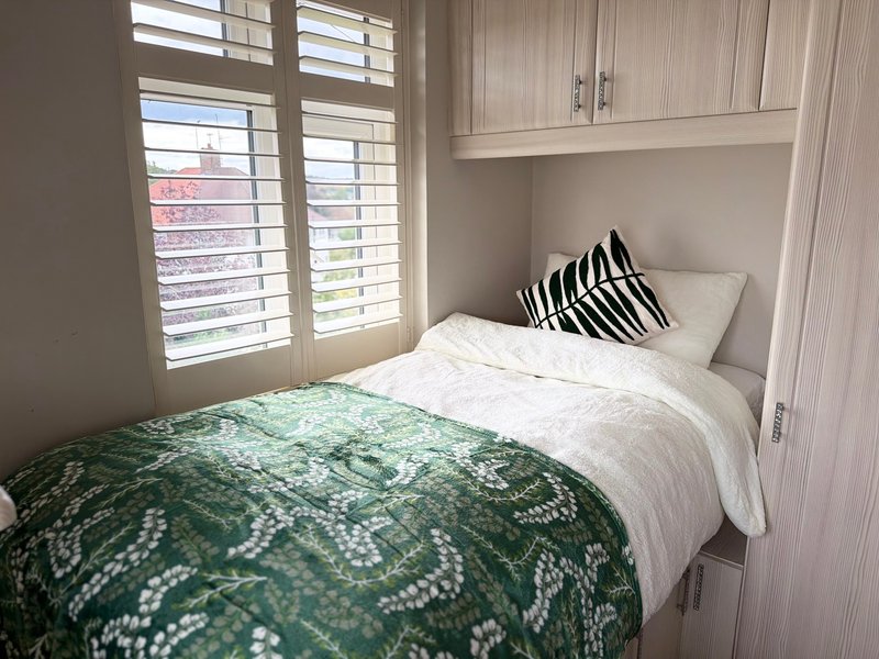 Bright bedroom with double bed, green patterned bedding, striped pillow, shuttered windows and built-in wardrobe