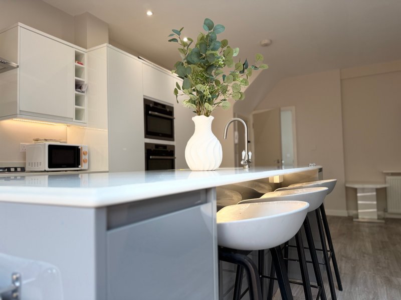 Modern white kitchen with island, bar seating, and white vase with greenery