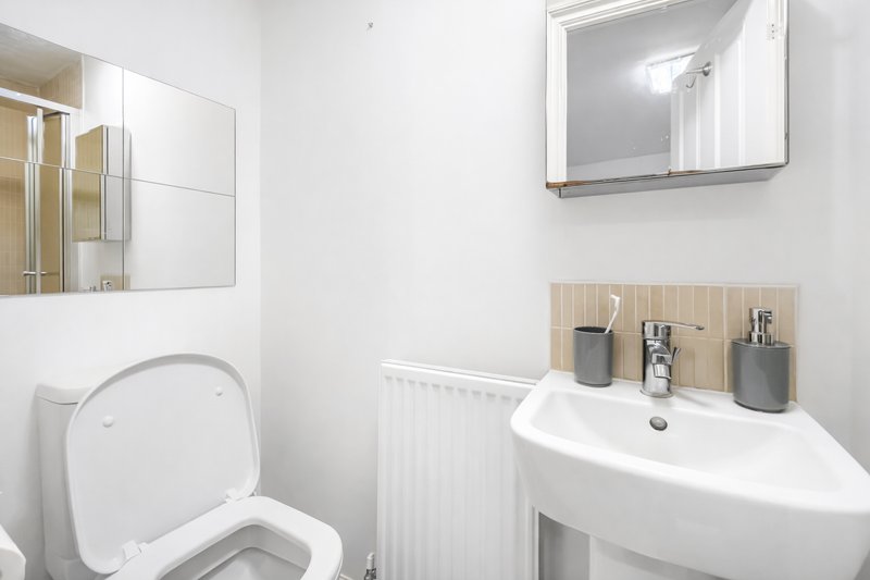 Modern bathroom with white toilet, curved sink, mirror and wooden shelf with toiletries