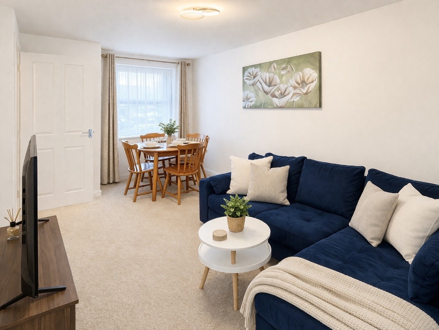 Bright living room with navy sofa, dining table, window with curtains and wall art