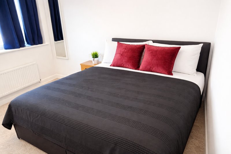 Bedroom with double bed, red and white pillows, black duvet, window with blue curtains