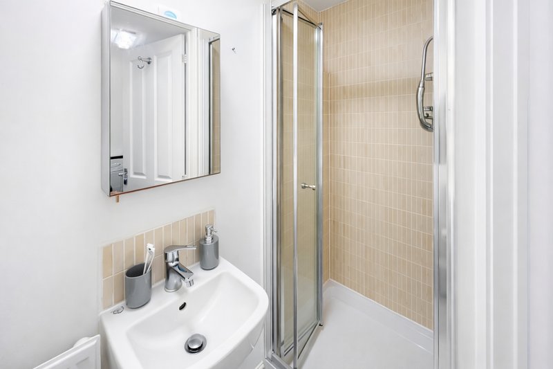 Modern bathroom with white sink, mirror, shower enclosure and beige tile walls