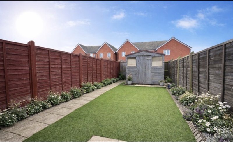 Enclosed brick garden with manicured lawn, wooden fencing, shed and flower borders