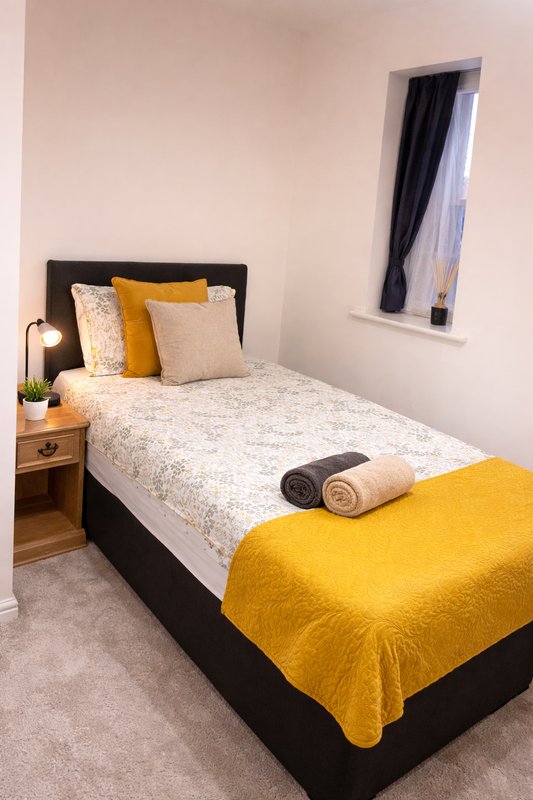 Bedroom with single bed, black headboard, yellow bedding, wooden bedside table and window