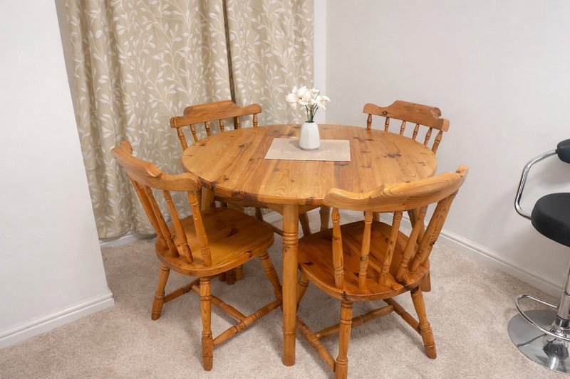 Dining area with round wooden table, four chairs, white flower vase, and beige curtains