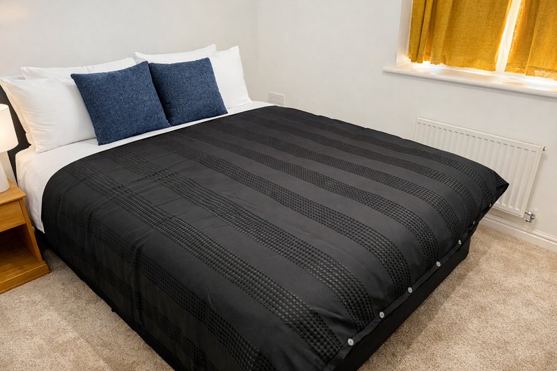 Bedroom with double bed, black duvet, blue pillows and wooden headboard