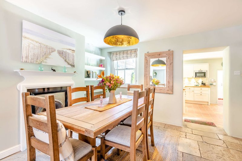 Bright dining room with wooden table, ladder-back chairs, black pendant light and open-plan kitchen view