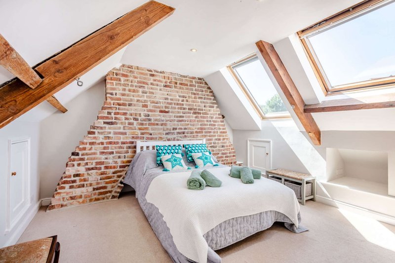 Attic bedroom with exposed brick wall, double bed, wooden beams and skylight windows