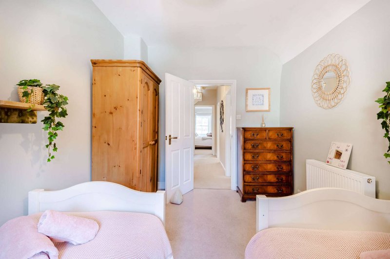 Bright bedroom with two single beds, wooden wardrobe, chest of drawers and potted plants