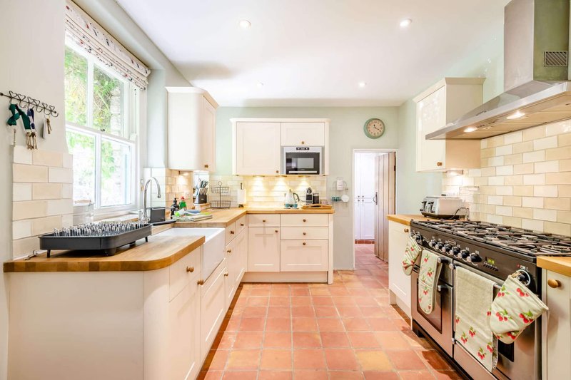 Bright kitchen with cream cabinetry, wooden countertops, range cooker and terracotta tile flooring