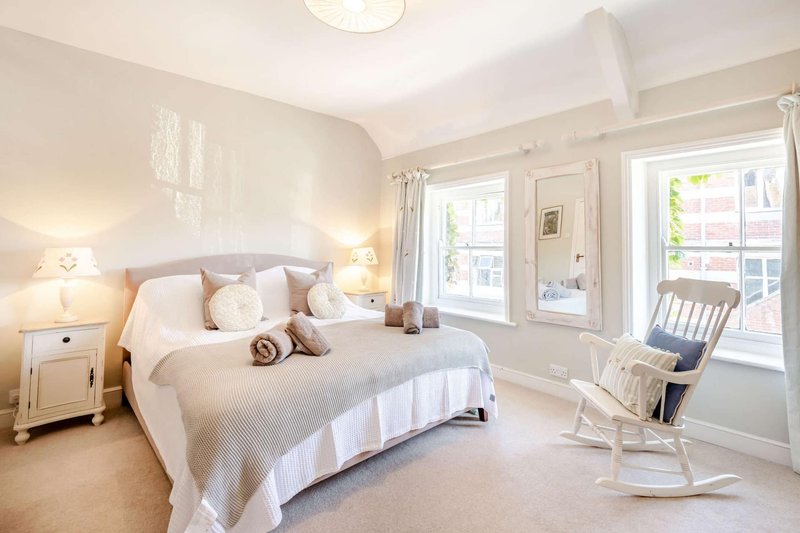 Bright bedroom with double bed, white bedding, bedside tables, rocking chair and patio doors