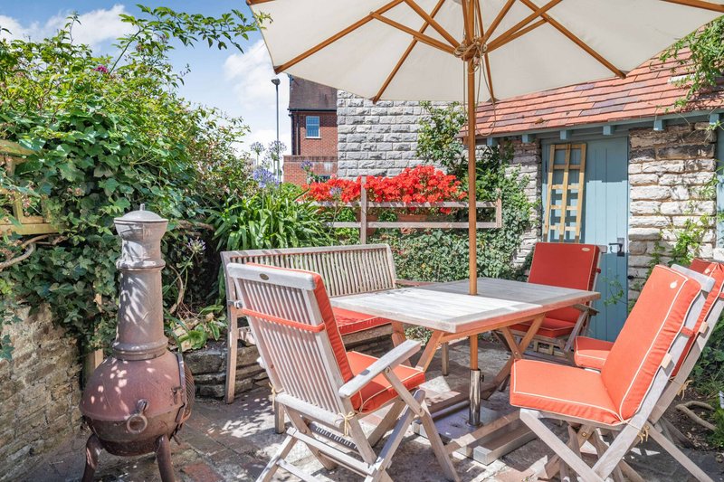 Outdoor patio area with wooden table, red chairs, umbrella, and stone cottage