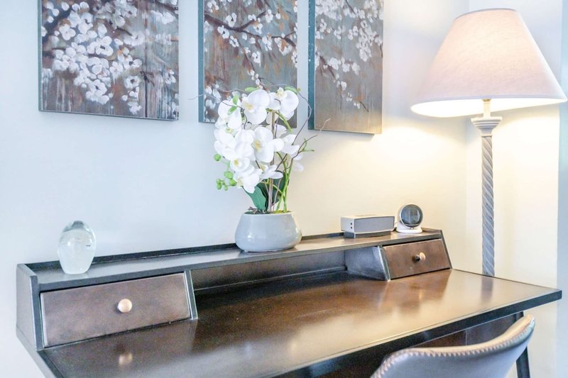 Wooden desk with drawers, white orchid arrangement, decorative artwork, and table lamp