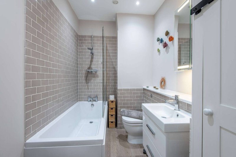 Modern bathroom with white subway tile, bathtub, toilet, sink and mirror
