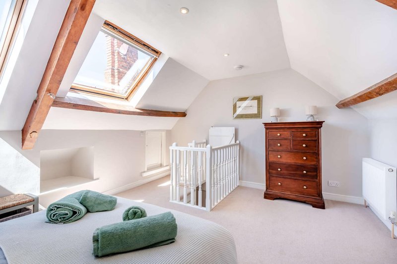 Bright attic bedroom with skylight, wooden beams, crib, chest of drawers, and green rolled towels on bed