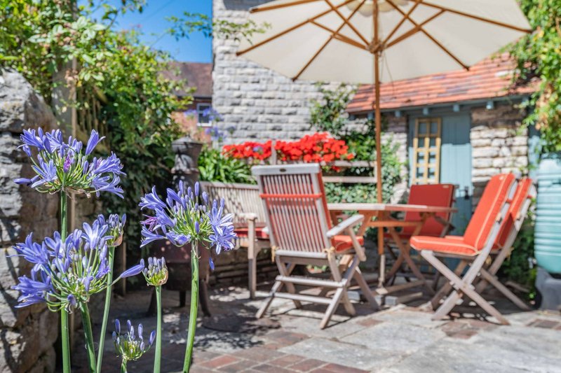 Garden patio with seating area, umbrella, flowering plants and stone cottage exterior