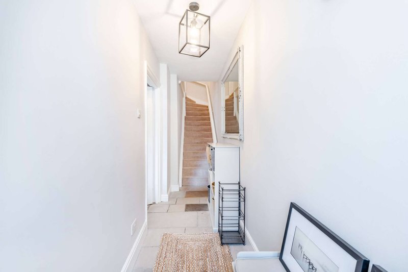 Bright hallway with white walls, wooden stairs, pendant light fixture and carpet runner