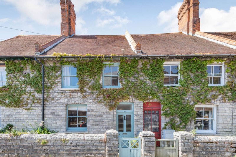 Stone terraced house with ivy-covered facade, blue door, and red postbox