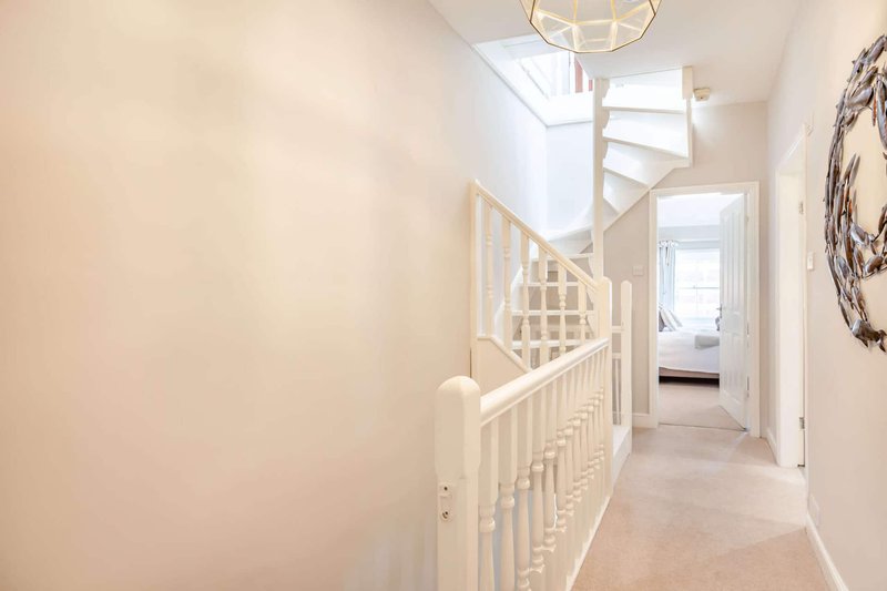 Bright hallway with white staircase railing, skylights, and open doorways leading to bedrooms