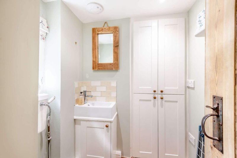 Bright bathroom with pedestal sink, wooden-framed mirror, white cabinetry and tiled backsplash