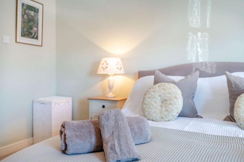Modern bedroom with double bed, grey headboard, patterned cushions, bedside lamp and folded towels