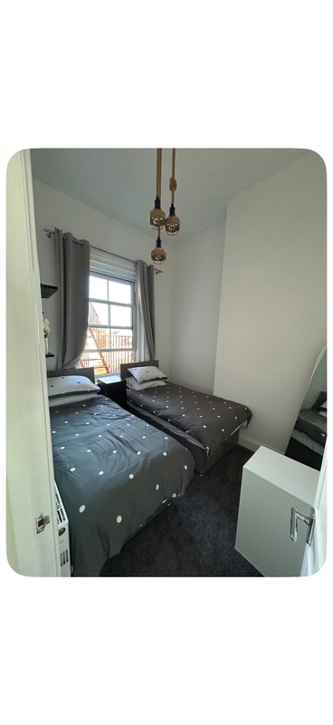 Small bedroom with single bed, pendant lights, window with curtains and dark flooring