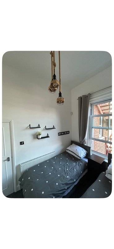 Compact bedroom with single bed, pendant lights, shelving, and large window with city view