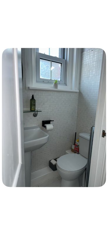 Compact bathroom with toilet, sink, window and tile walls