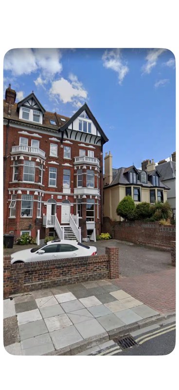 Red brick Victorian townhouse with white trim, front garden, and paved driveway on residential street