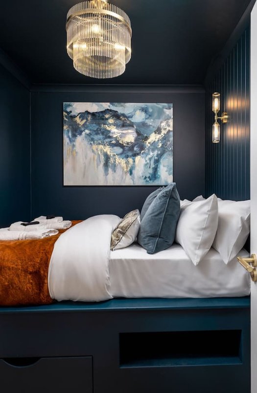 Modern bedroom with dark navy walls, pendant light fixture, and bed with white linens and decorative pillows