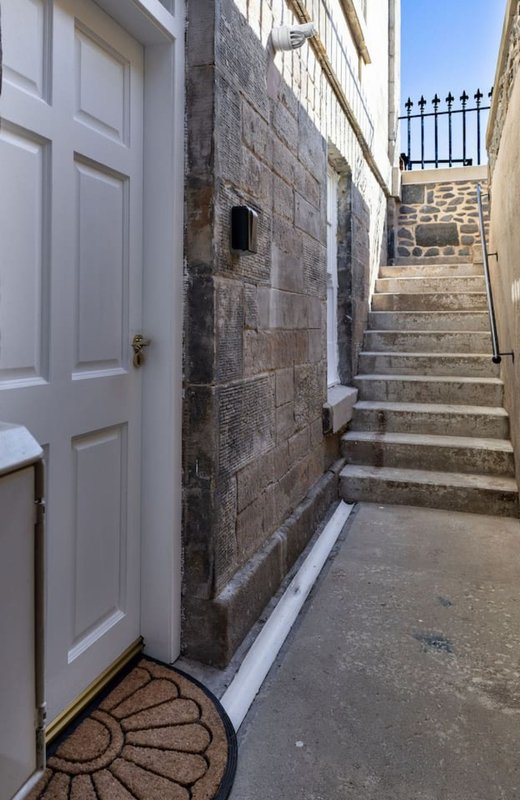 Entrance doorway with white door, stone wall exterior, and stairs leading upward