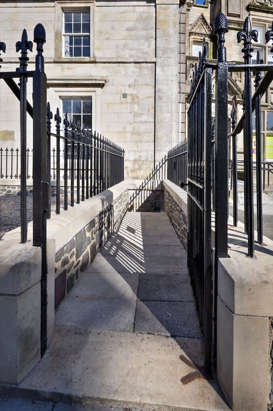 Stone building entrance with black iron gates and railings leading to front door