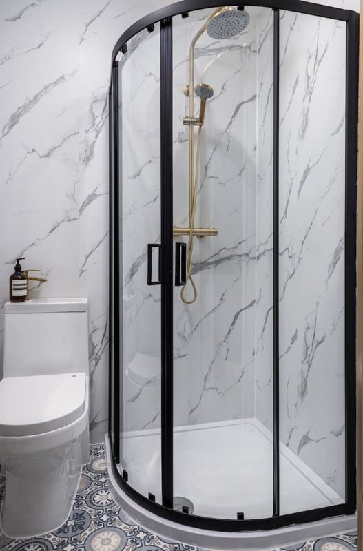 Modern bathroom with curved glass shower enclosure, marble-effect walls, and toilet
