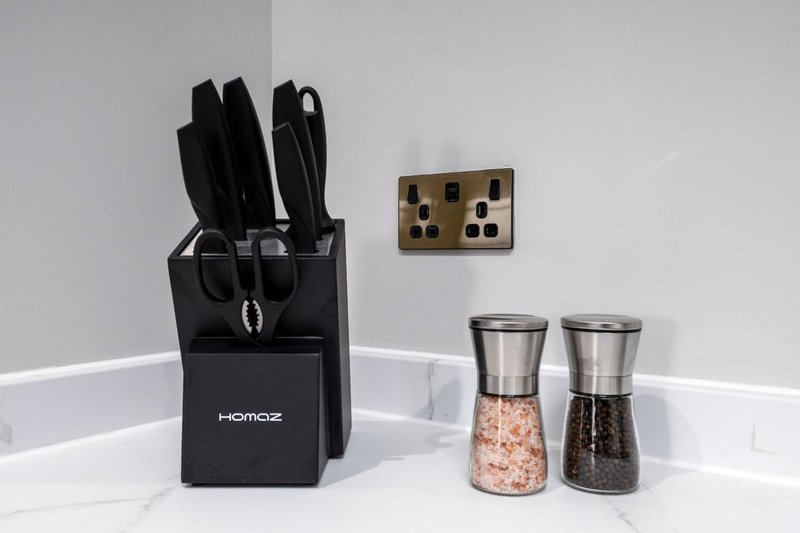 Kitchen counter with knife block, salt and pepper shakers, and brass outlet on white wall