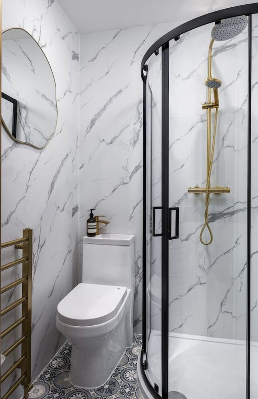 Modern bathroom with marble-effect walls, toilet, walk-in shower, brass fixtures and heated towel rail