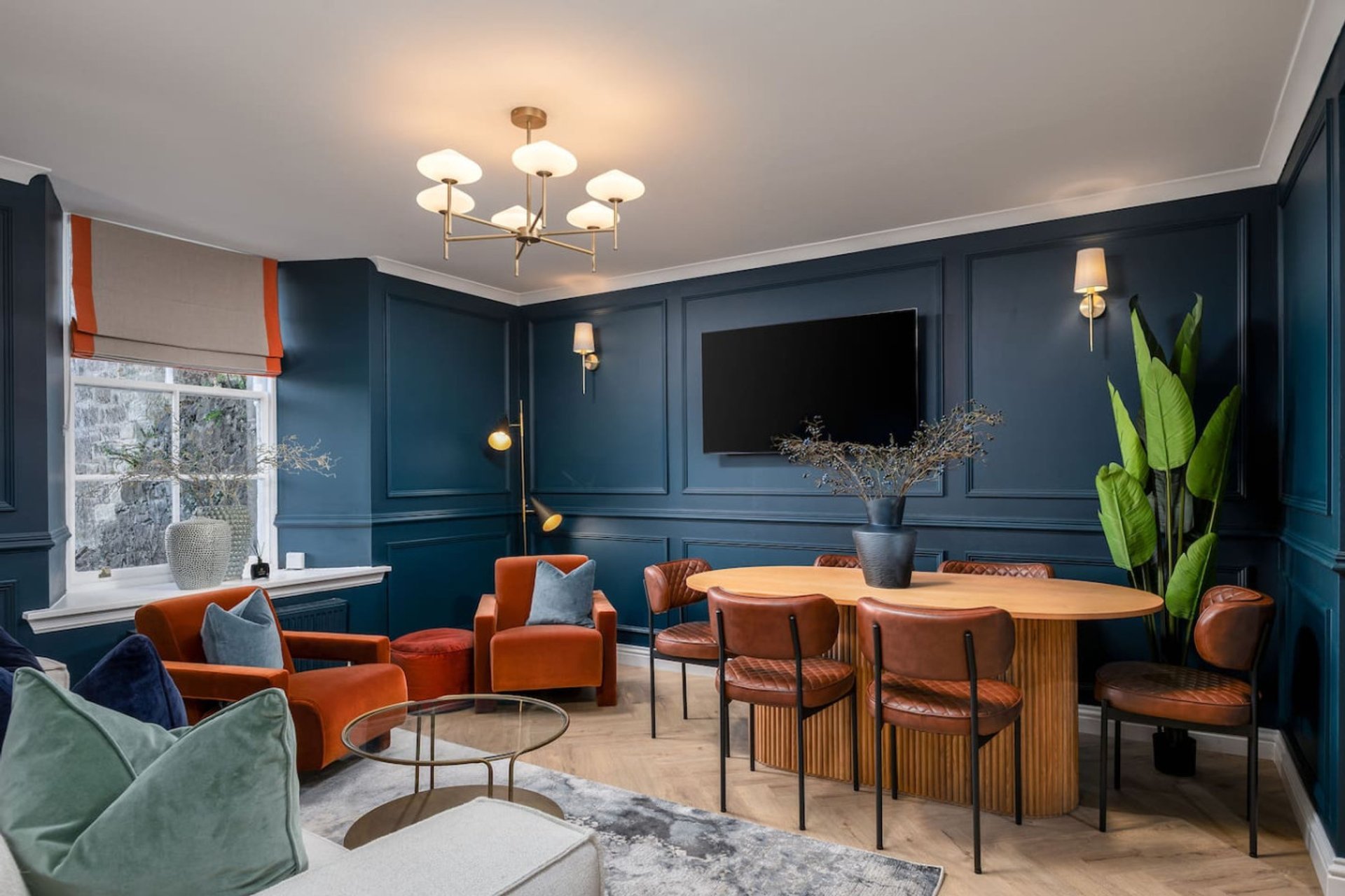 Open-plan living and dining room with blue walls, orange armchairs, wooden dining table and chairs