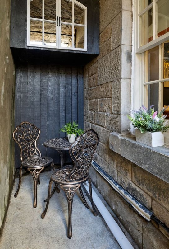 Narrow exterior courtyard with two ornate metal chairs, small round table and potted plants