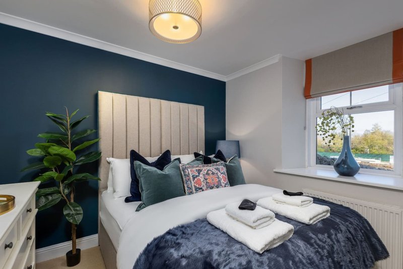 Modern bedroom with double bed, teal accent wall, cushions, and window with garden view