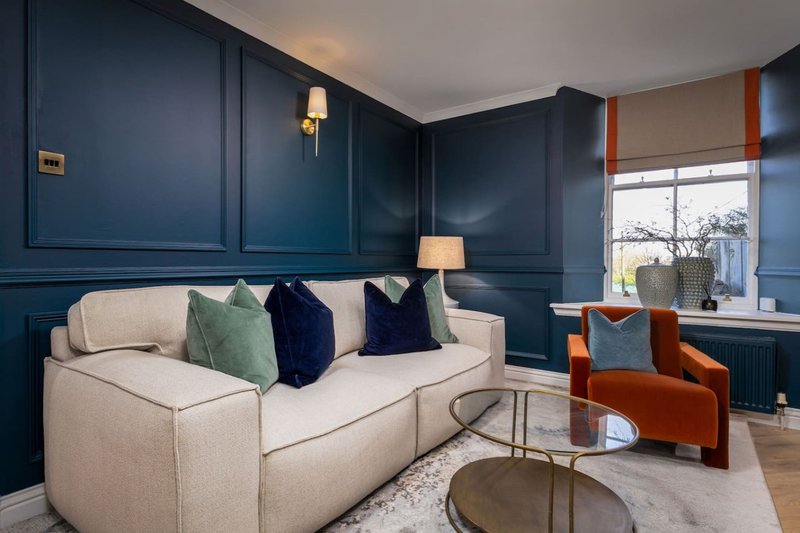 Modern living room with cream sofa, blue paneled walls, orange armchair and side tables