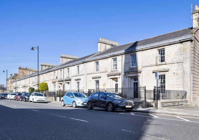 Row of Georgian stone townhouses with parked cars on street, clear blue sky