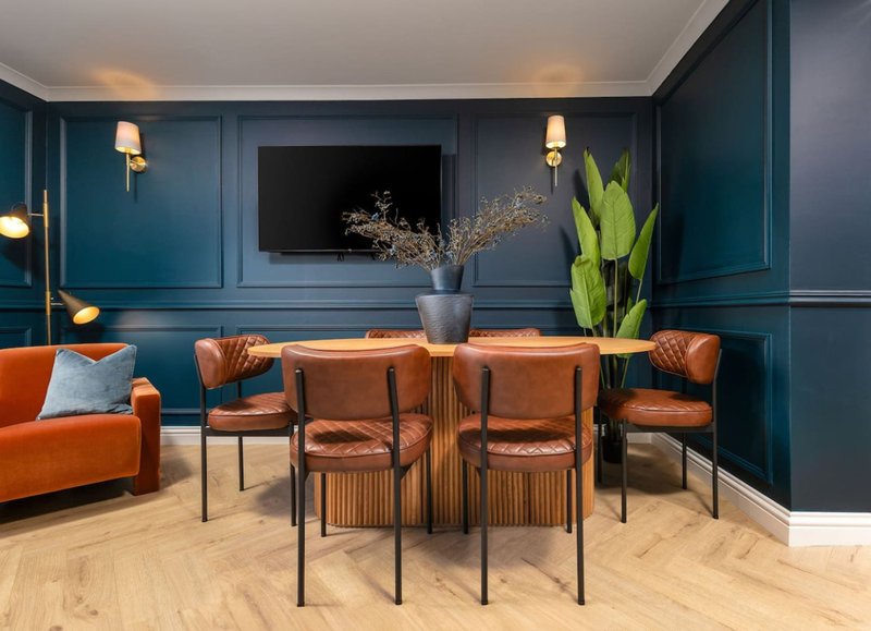 Modern dining room with wooden table, orange chairs, teal paneled walls and mounted TV