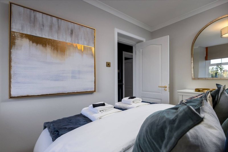 Modern bedroom with double bed, white bedding, dark pillows, framed abstract artwork and round mirror