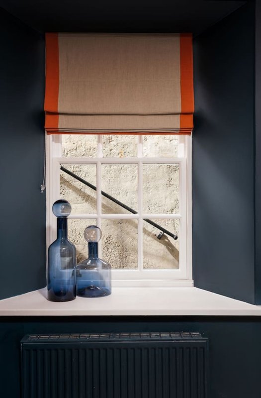 Window with roman blind, decorative blue bottles and branches on white windowsill
