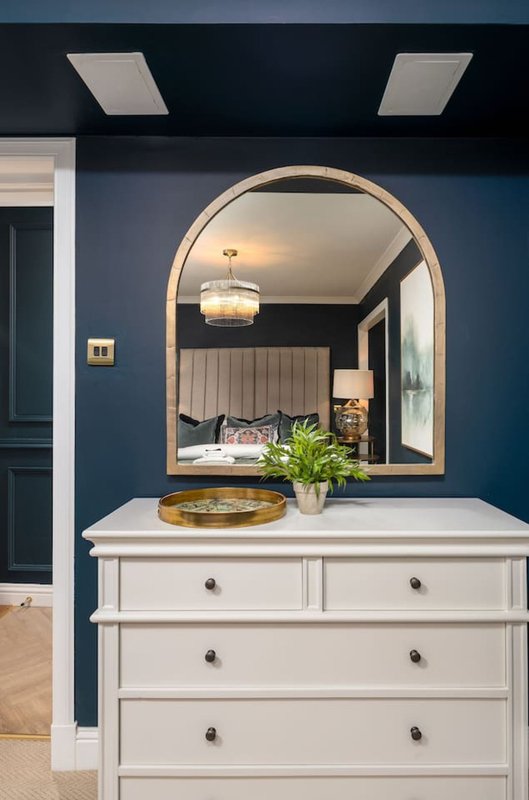 Modern bedroom vanity with arched mirror, white dresser, potted plant and pendant lighting