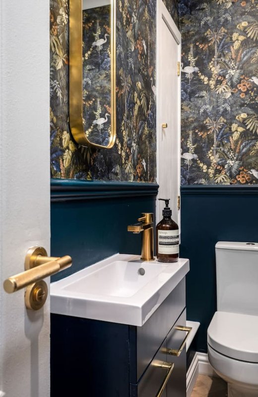 Modern bathroom with white sink, dark blue vanity, gold fixtures and patterned wallpaper