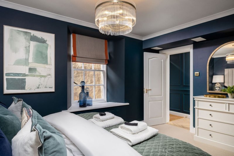 Modern bedroom with navy walls, double bed, white dresser, chandelier and window