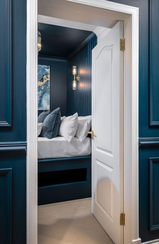 Modern bedroom with dark blue walls, white bedding, pendant lights, and framed artwork