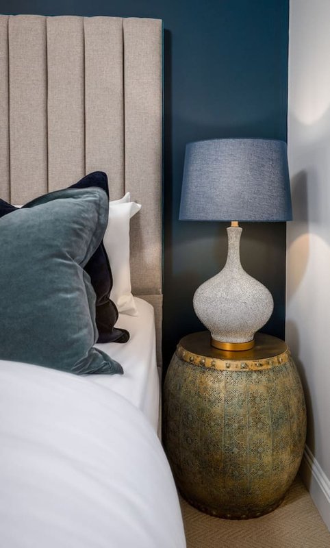 Modern bedroom with upholstered headboard, decorative pillows, bedside table lamp and gold accent table
