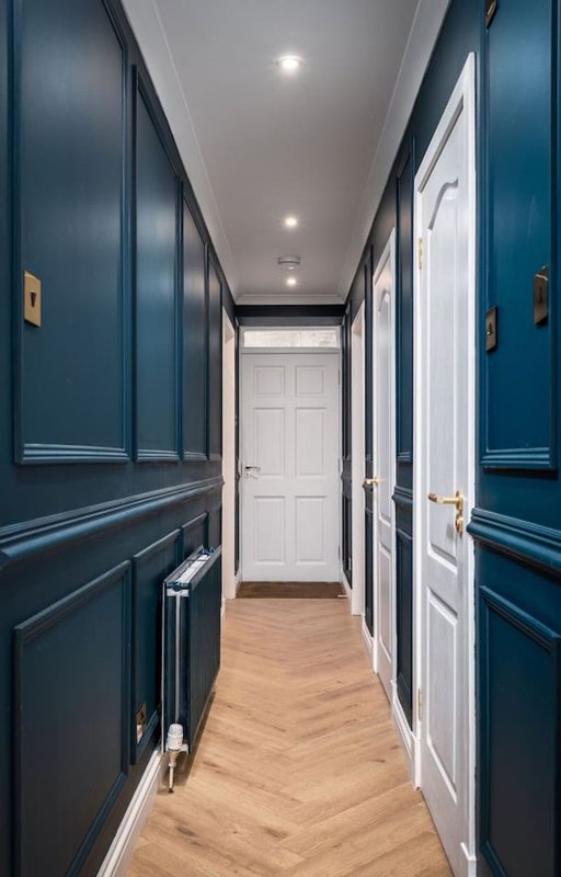 Narrow hallway with dark blue panelled walls, white doors, recessed lighting and wooden floor